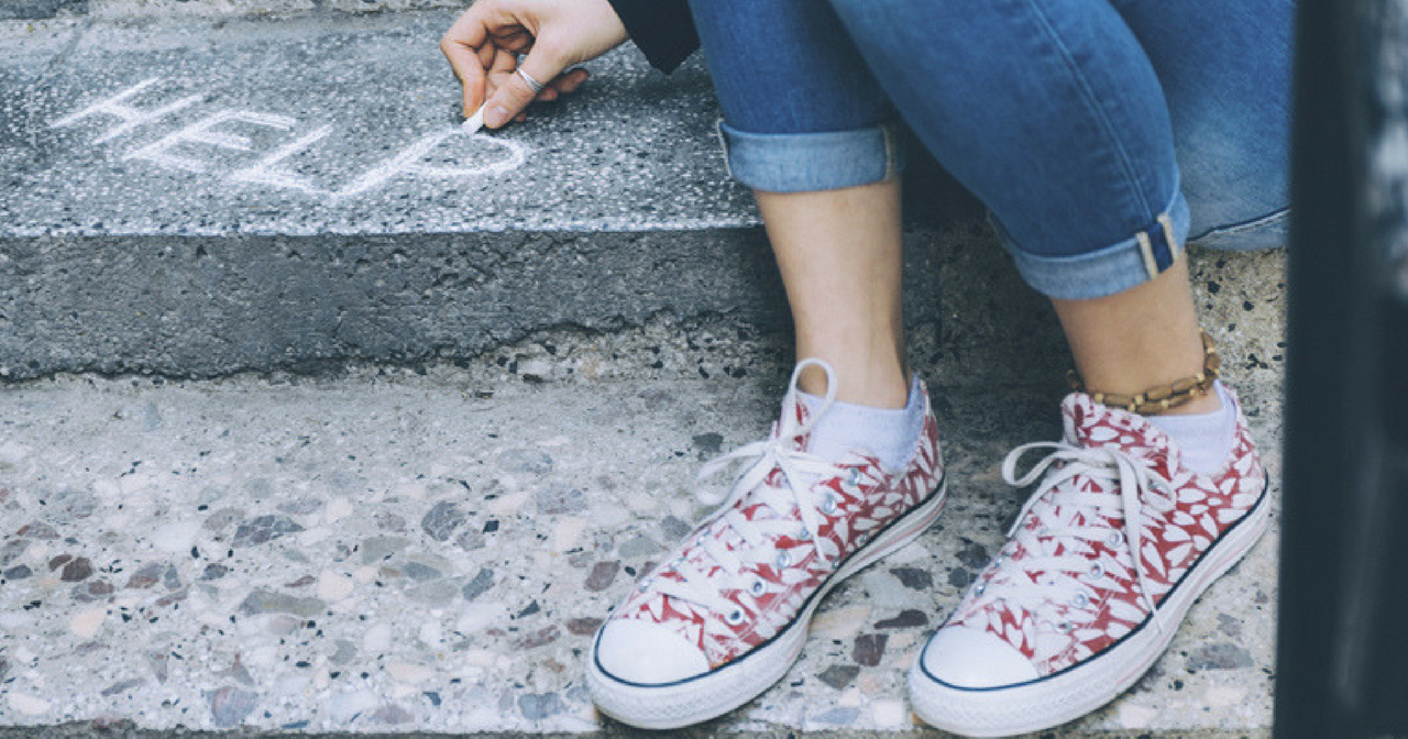 a woman drawing the word HELP in chalk on the sidewalk