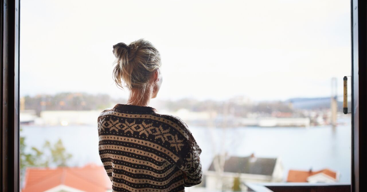 A woman with her back to the camera looks out a window 