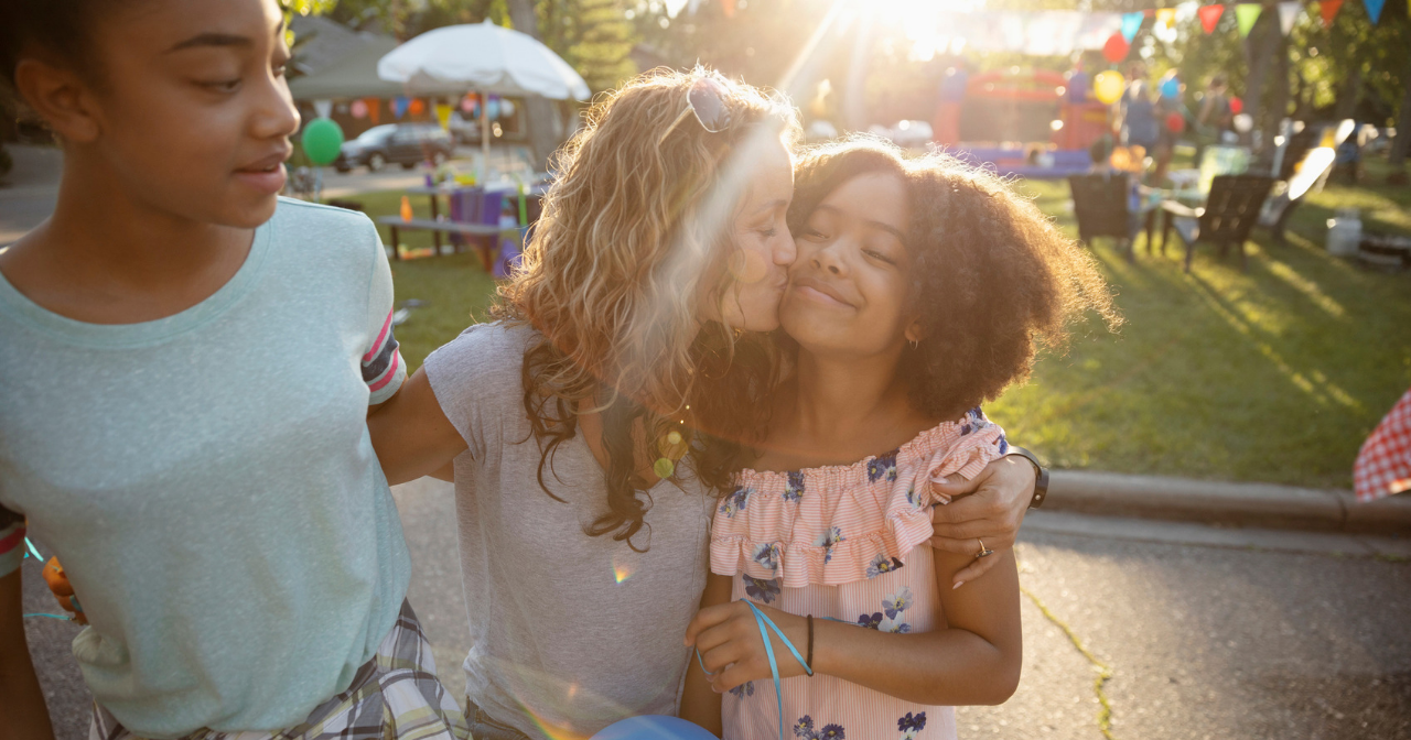 A mother kisses one daughter while hugging other daughter.