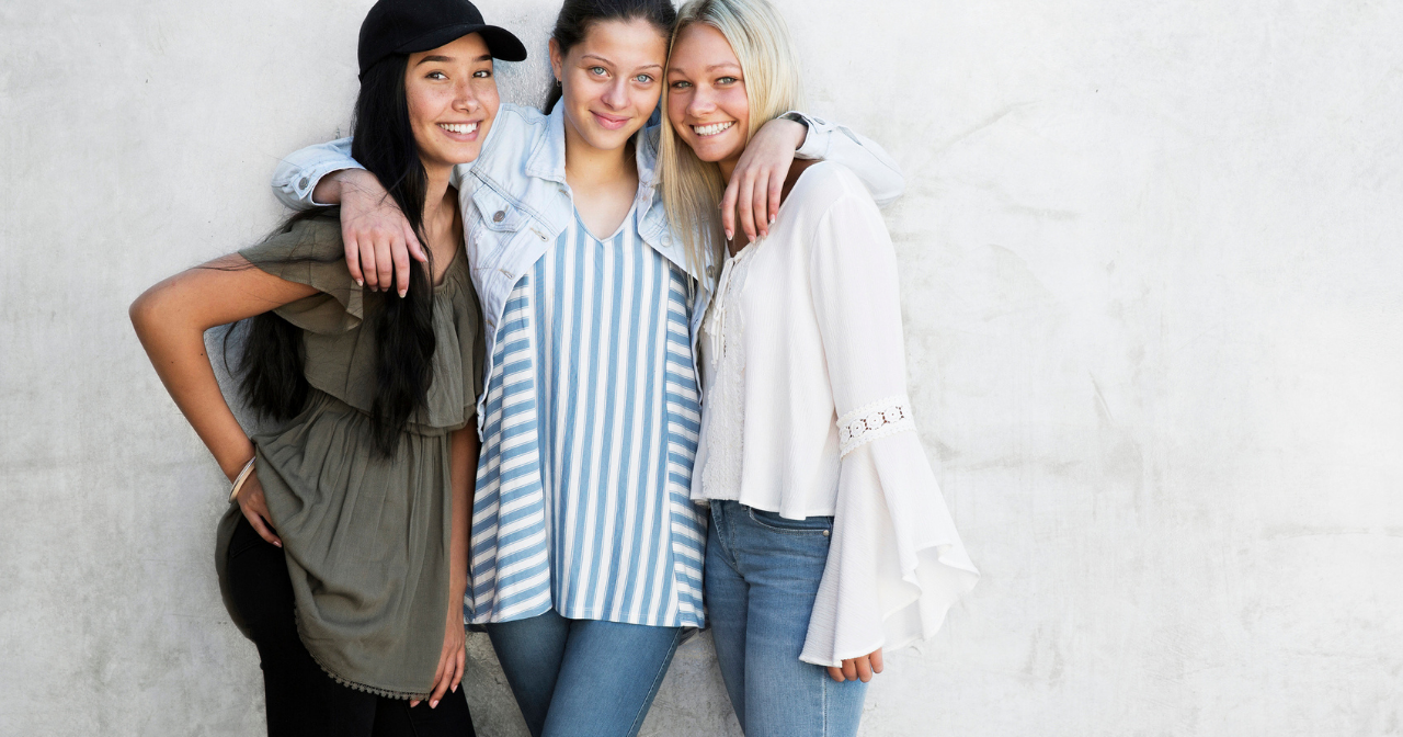 Three young women pose for a picture with their arms around each other and big smiles. 