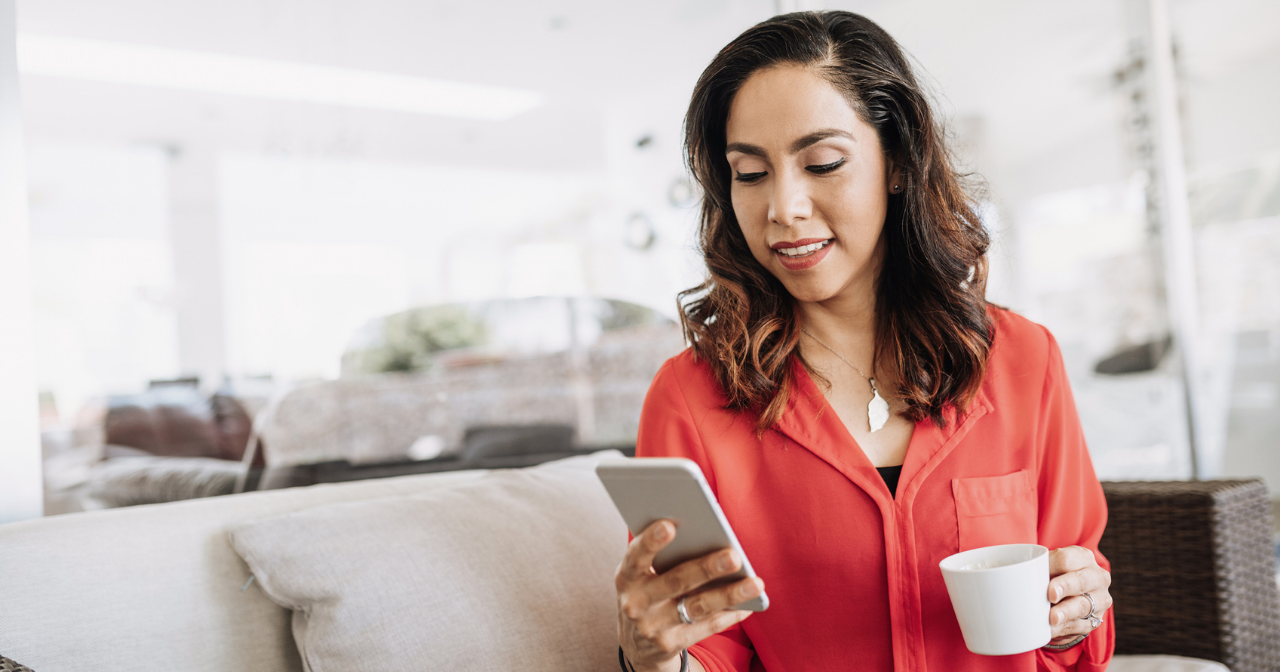 A woman sits on her sofa with a cup of coffee and her phone. 