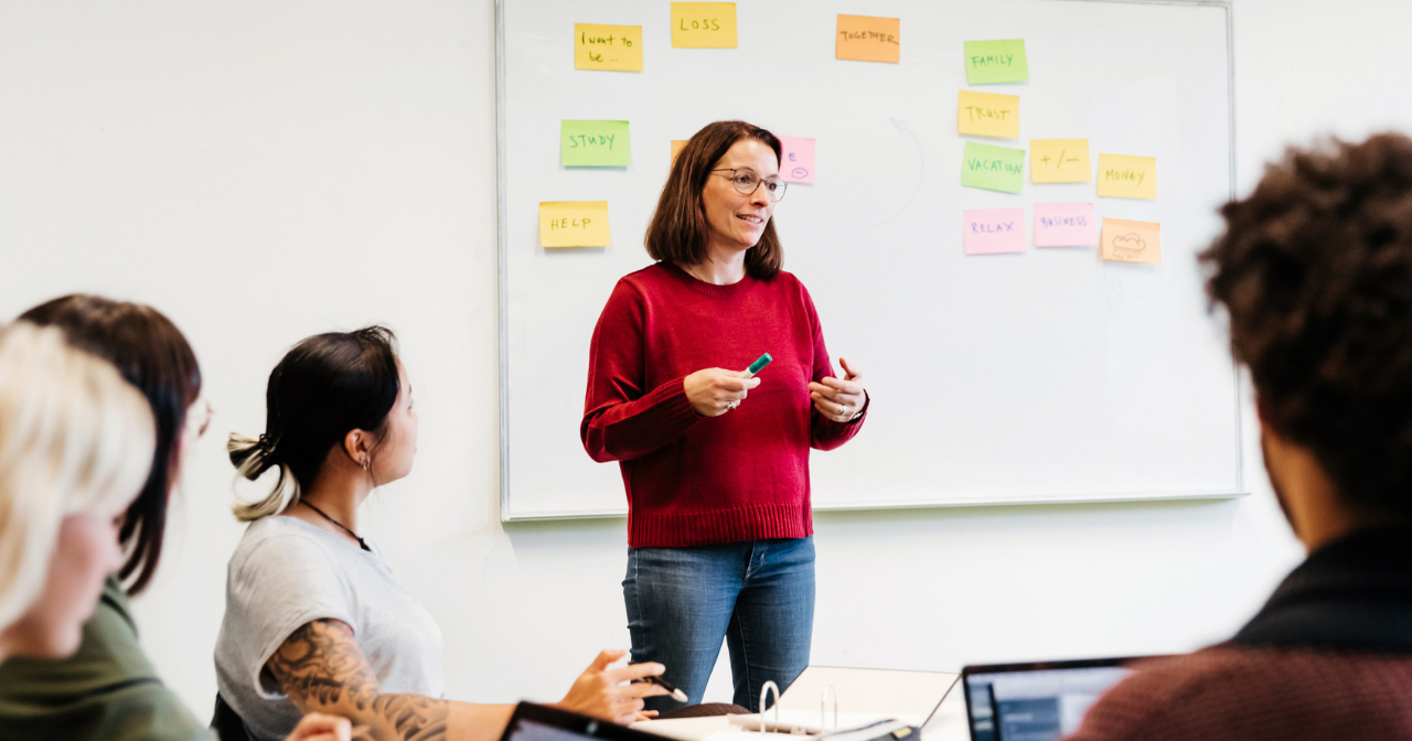 A teacher stands at the front of a classroom and engages her students in a discussion. 