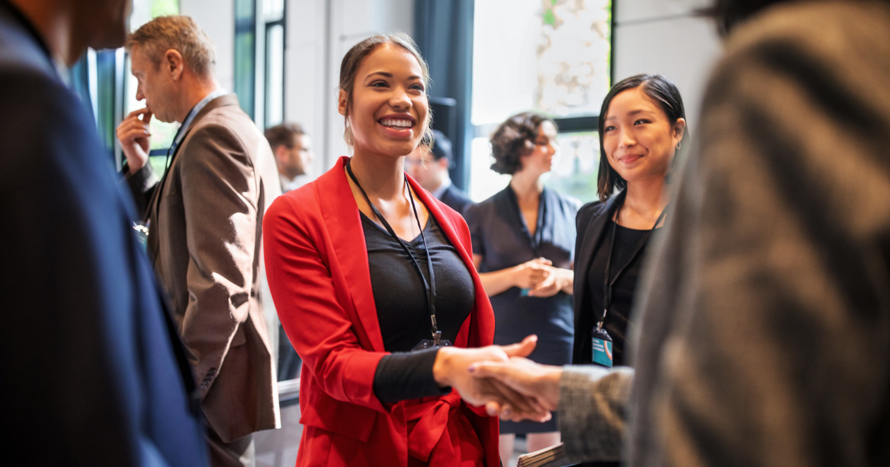 A woman in a red jacket shakes hands with someone at an event. 