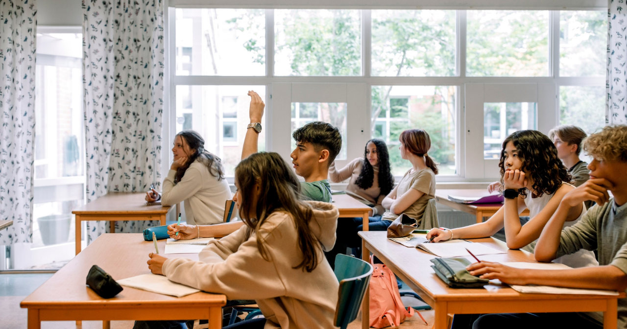 A class of teens sitting forward and listening to a teacher. 