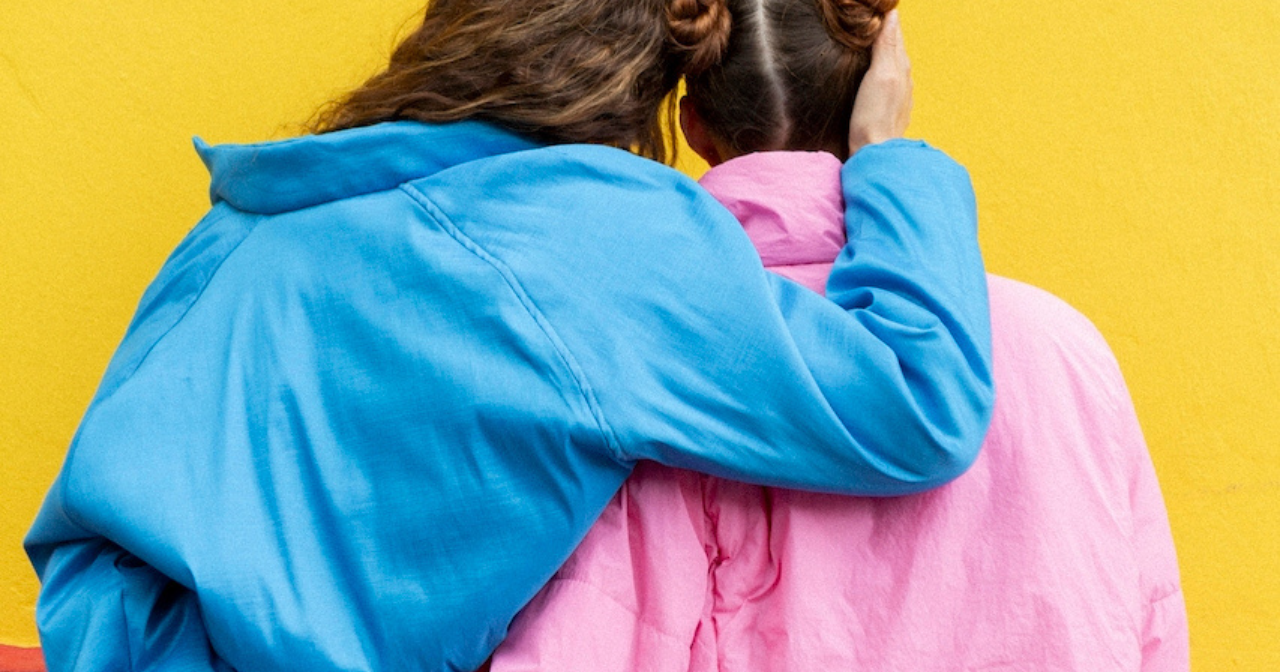 A photo of the back of two women in love who are hugging one another. 