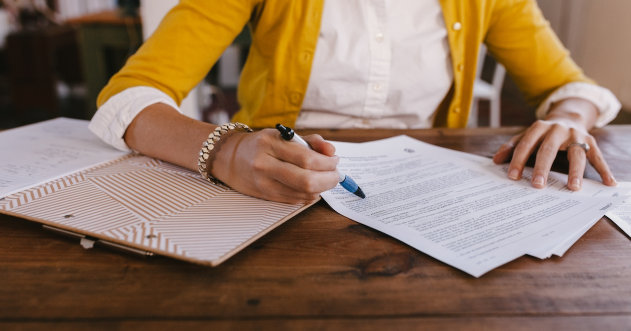 A photo of a woman signing some papers on a desk. 