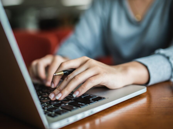 A woman holds a pen and types on a laptop