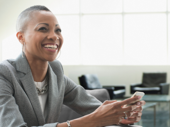 A woman in a suit holds her phone and smiles