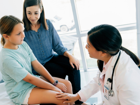 A mother and daughter sit in an exam room with a provider. 