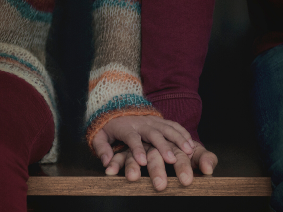 A woman's hand rests on top of her partner's on a bench.