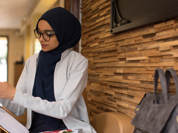 A provider wearing a hijab while sitting on a bench and reviewing information. 