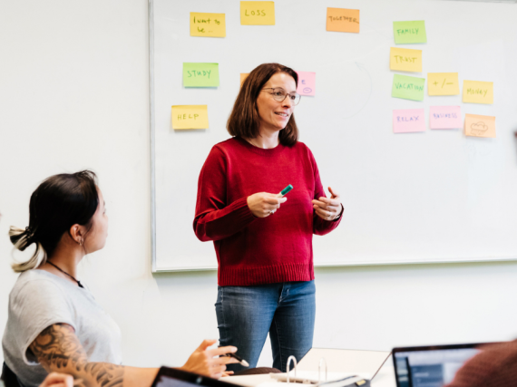 A teacher stands at the front of a classroom and engages her students in a discussion. 