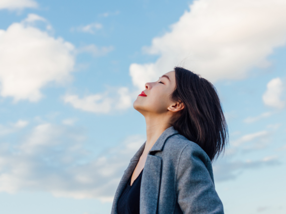 A woman looks up at the sky with a contented smile and closed eyes. 