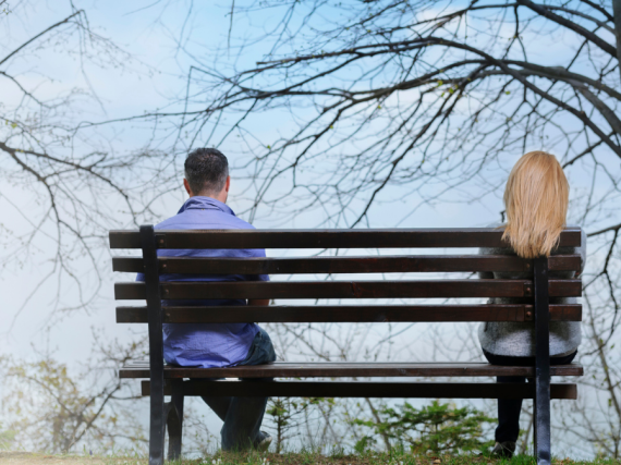 A couple sits on either end of a bench in a park. 