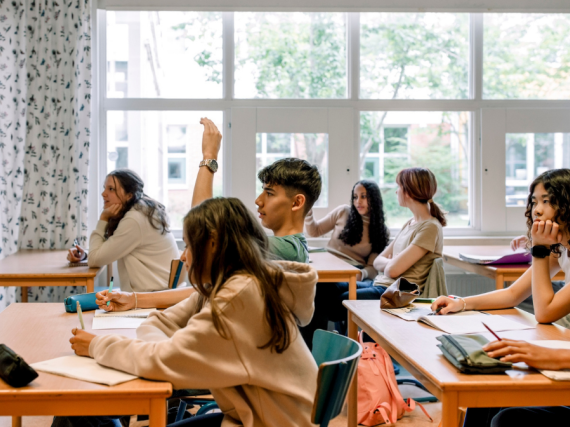 A class of teens sitting forward and listening to a teacher. 