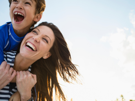 A son sits on his mom's back and the two laugh.