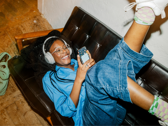 Person looking at phone and smiling with their feet up and on the couch.